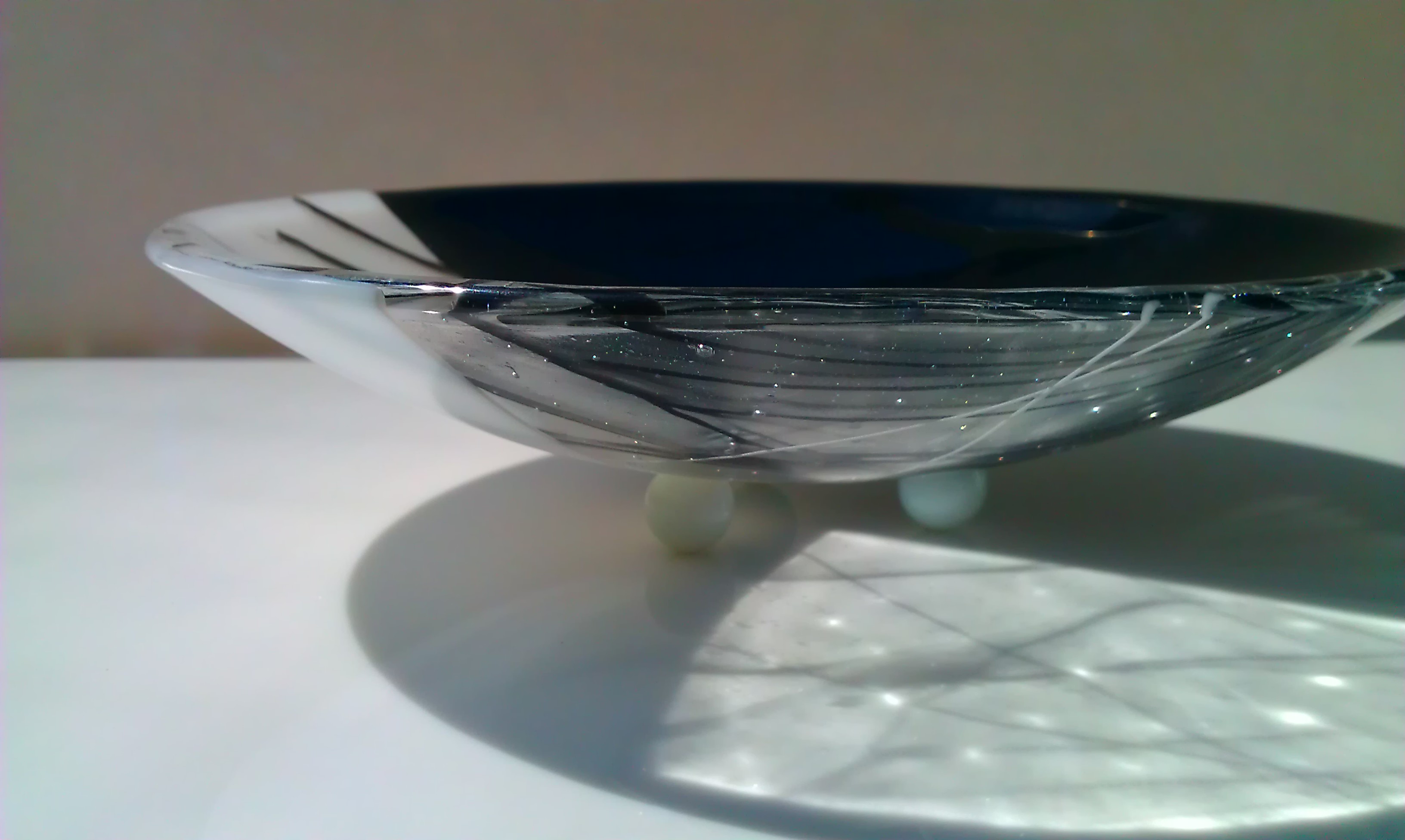 This black and white bowl is footed.  The contrast of white black and clear is striking. The light shines through the clear and reflects the textures in the glass.  